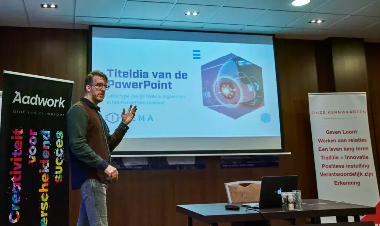 Aad Wagner van Aadwork geeft een presentatie over PowerPoint in een vergaderruimte met banners van zijn bedrijf.